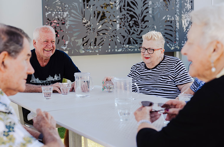 A small group of family members and carers sitting together in a quiet café-style space, talking and offering support during a Dementia Connections Café meetup.